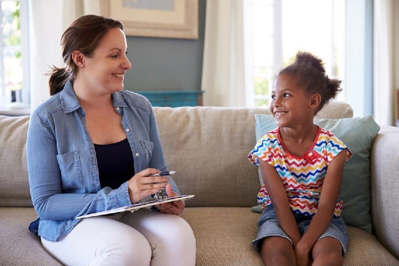 A little girl sits on a sofa and chats with a woman who's a counselor. Stock Photo