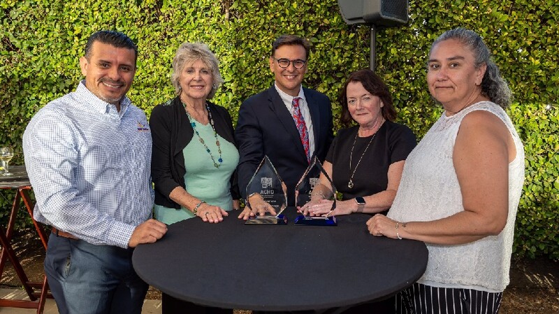 Members of the Desert Healthcare District and Foundation Board and staff stand with the ACHD CEO at a table topped with two awards. Submitted Photo