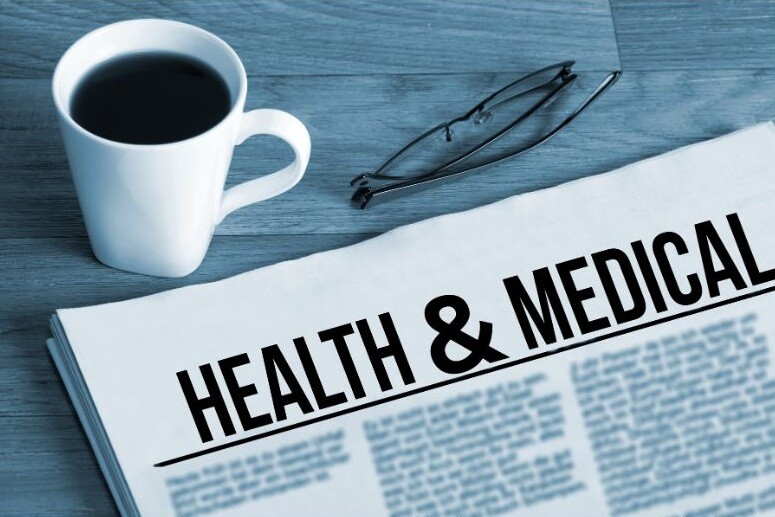 We see a newspaper with the headline "Health & Medical" on a table near a cup of coffee and folded reading glasses. Stock Photo