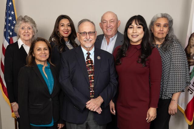 The Board members stand as a group of two rows between the California state flag on one side and the American flag on the other. Photo by Lani Garfield