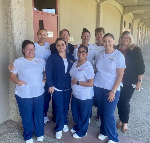 Two rows of College of the Desert registered nursing students standing and facing the camera, with agency CEO Chris Christensen, CPO Donna Craig and a female college official standing in the back row with two students.