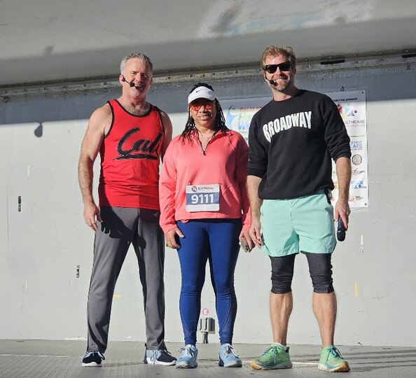 District staff member Andrea Hayles (center) stands on stage with fitness instructors Scott Cole (left) and Craig Ramsay (right). All face the camera.