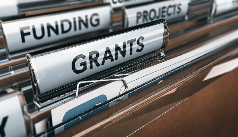 A row of brown standing file folders that are labeled with black ink on white paper. The labels including "Grants" and "Funding."