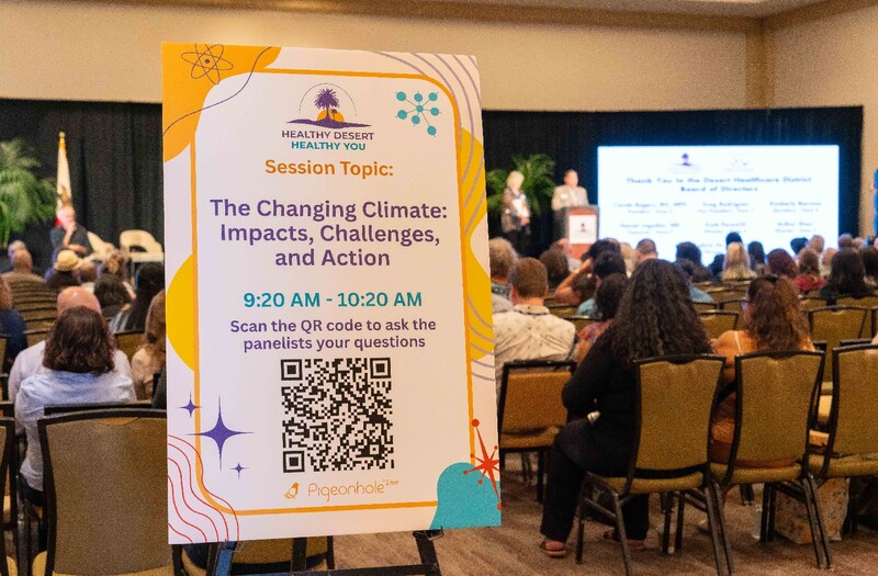 A colorful poster board on an easel announcing a summit session (in the foreground) and the back of a seated audience looking toward the stage in the background. Staff Photo
